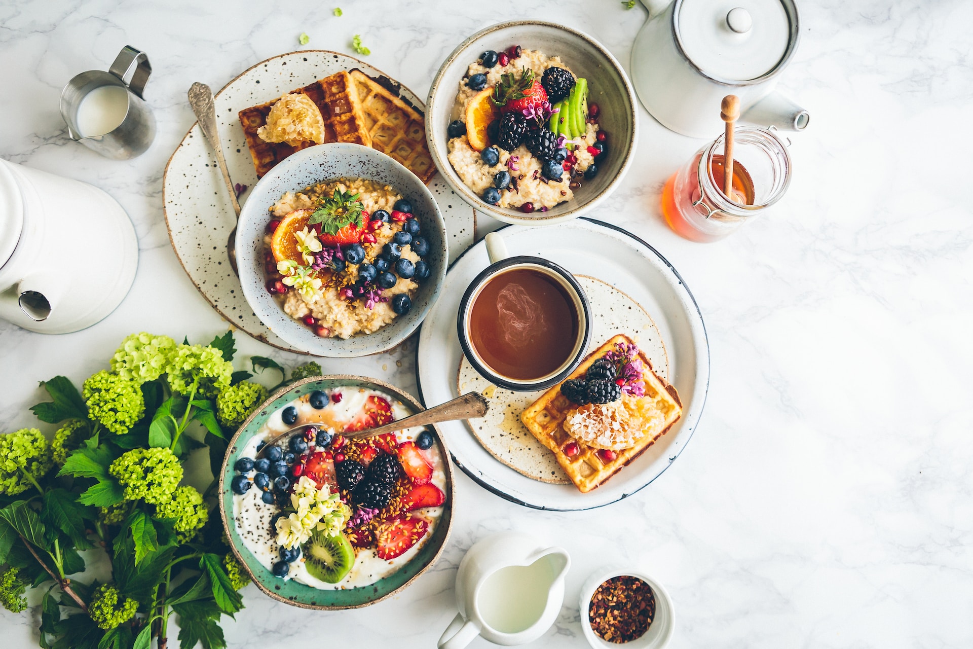 A table set with breakfast items including bowls of oatmeal with fruit, waffles, and cups of coffee.